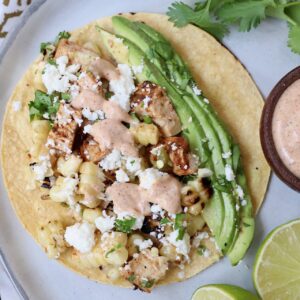 taco on plate topped with diced chicken, corn kernels and avocado slices