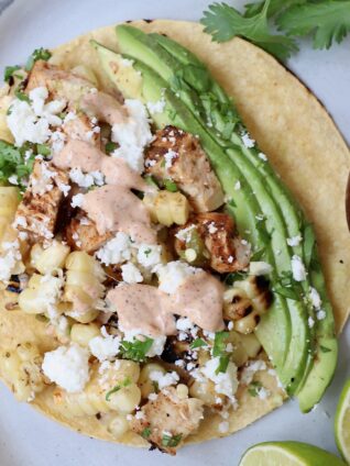 taco on plate topped with diced chicken, corn kernels and avocado slices