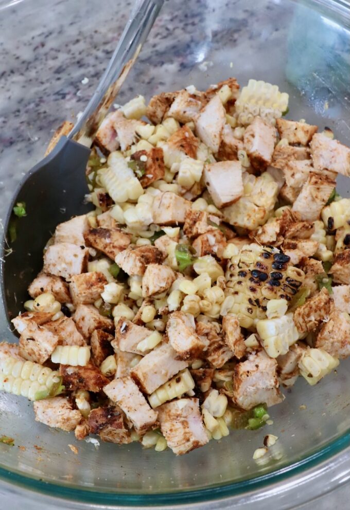 diced grilled chicken, corn kernels and diced jalapenos in glass bowl with mixing spoon