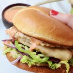 hand holding buffalo chicken smash burger over a plate