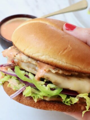 hand holding buffalo chicken smash burger over a plate