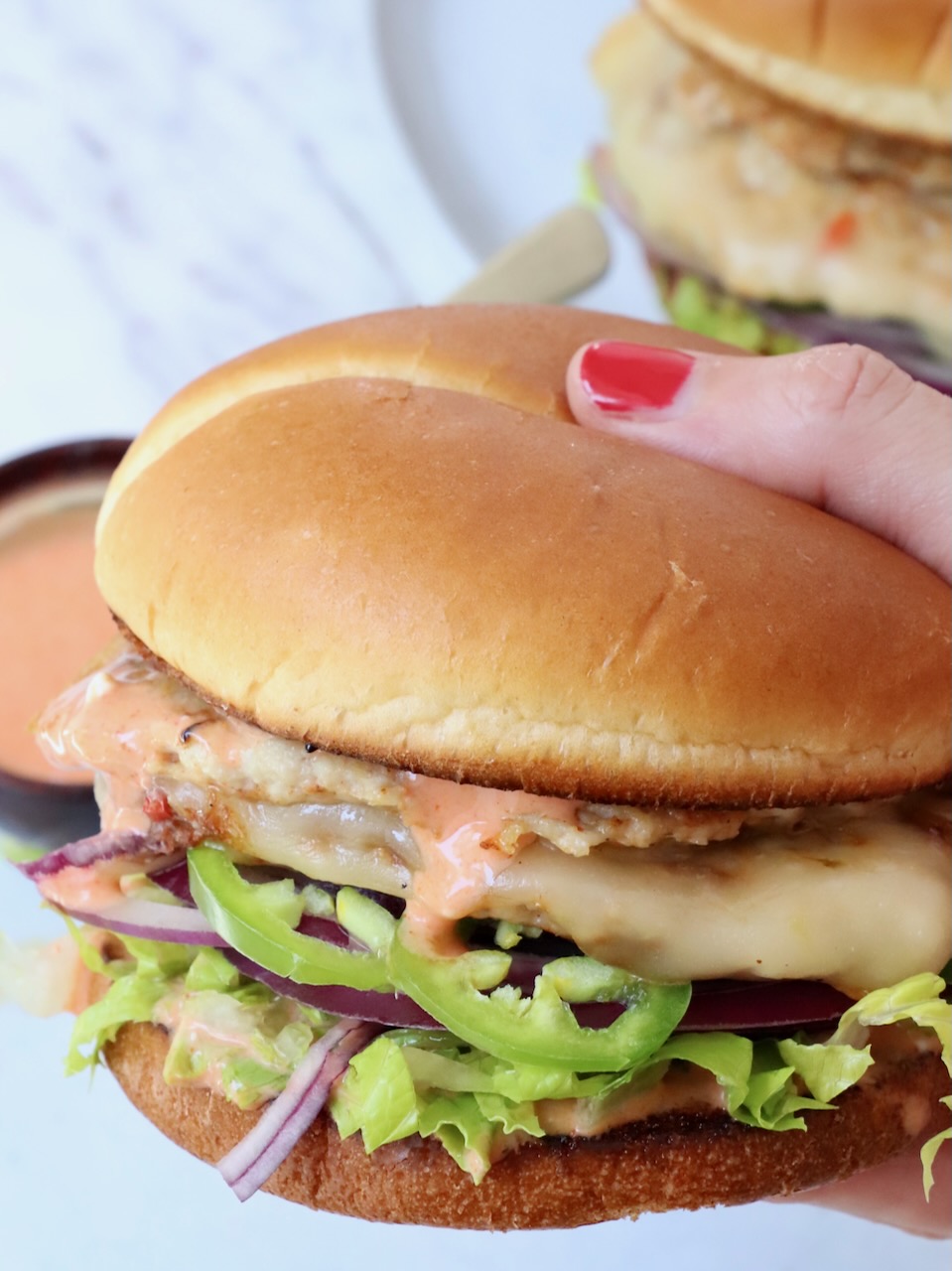 hand holding chicken smash burger over plate