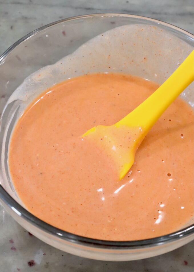 buffalo sauce and blue cheese dressing combined in a glass bowl with a yellow spatula