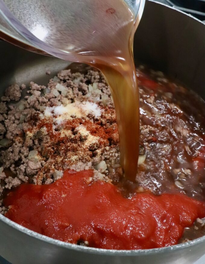 beef broth poured into a pot with cooked ground beef, spices and tomato sauce