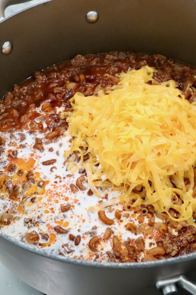 shredded cheddar cheese and heavy cream in a pot of cooked ground beef, noodles and sauce