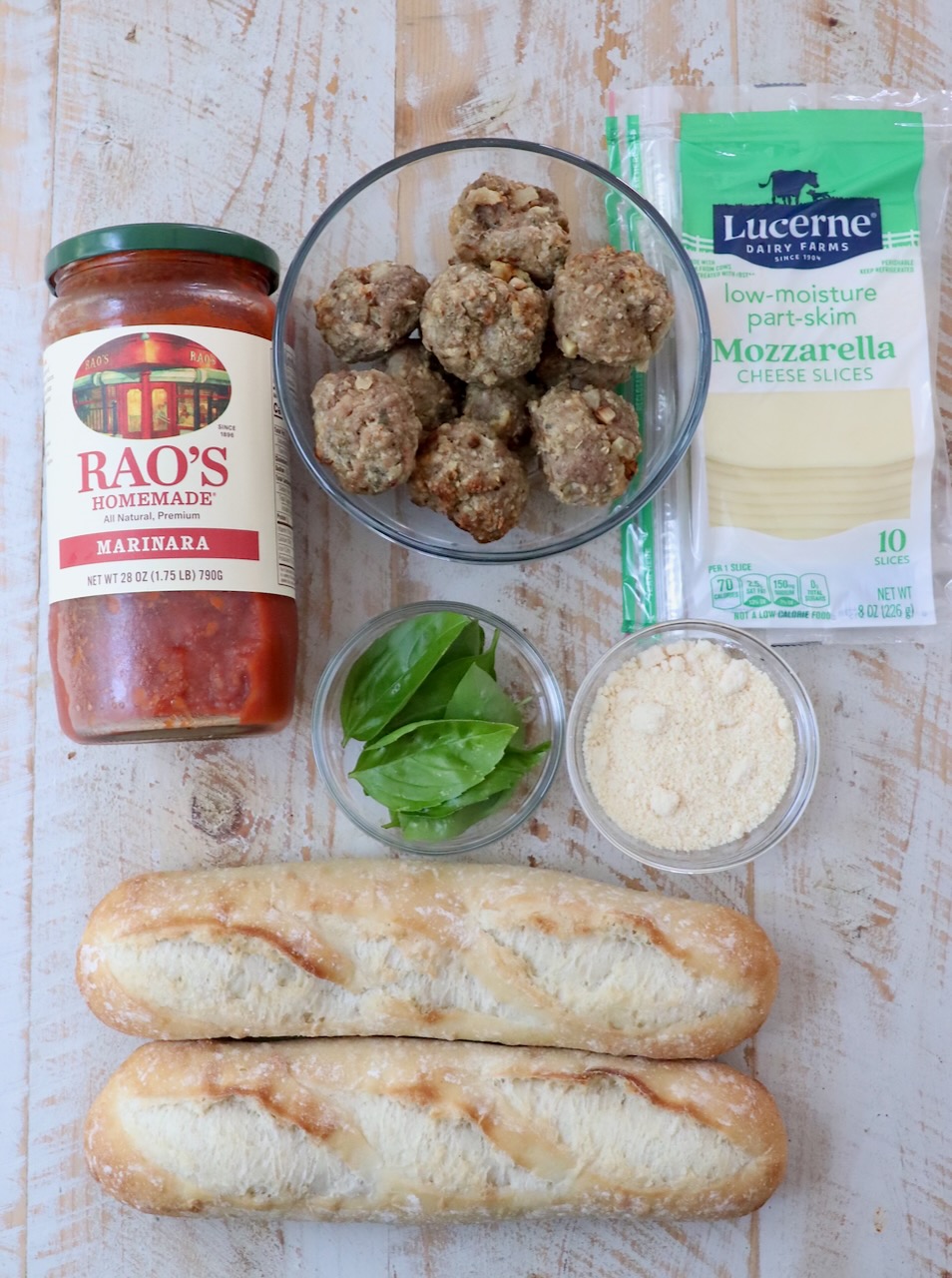 ingredients for meatball subs on white wood board