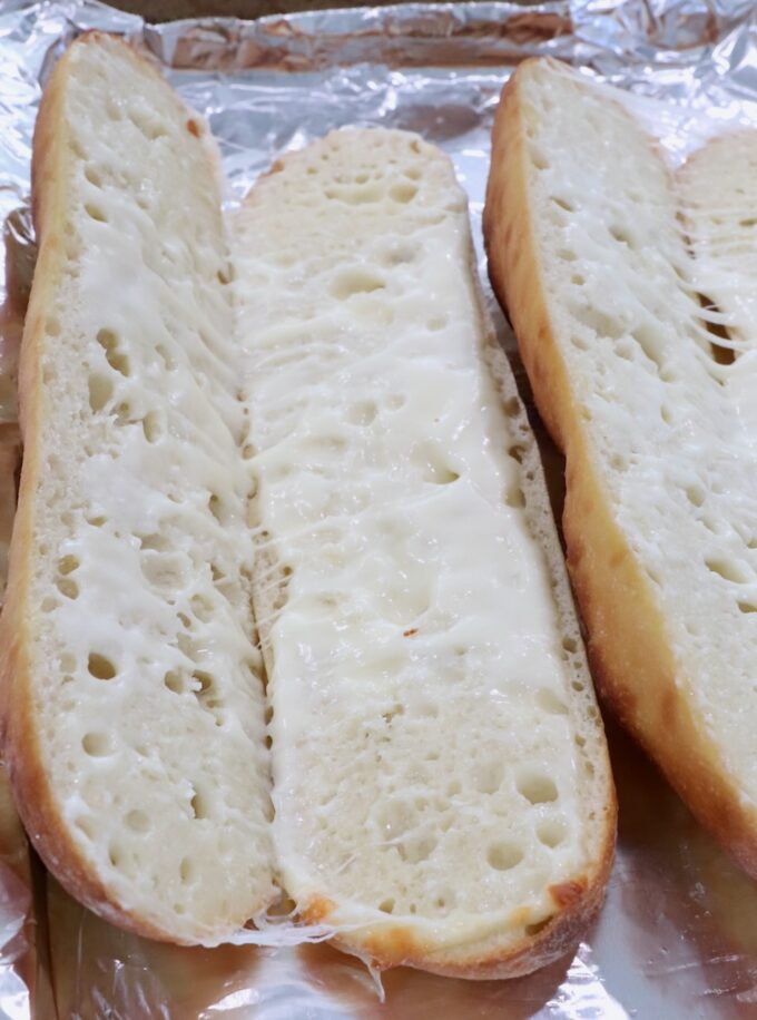 melted cheese in a baguette sliced in half on a foil lined baking sheet