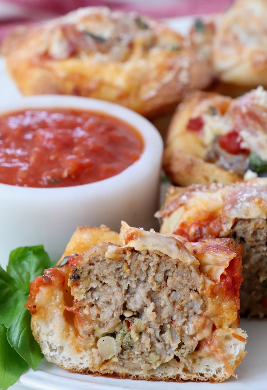 meatball sub bites cut in half on plate with marinara sauce in a bowl on the side