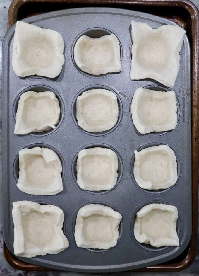 pizza dough squares pressed into a muffin tin