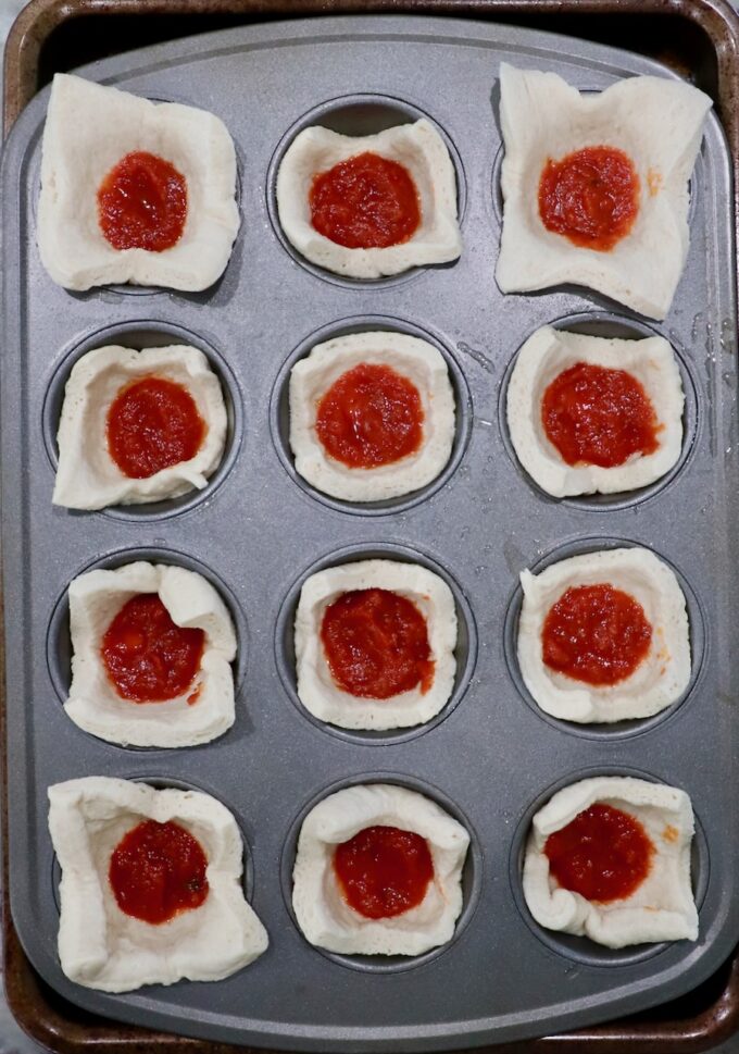 pizza dough squares pressed into a muffin tin and filled with marinara sauce