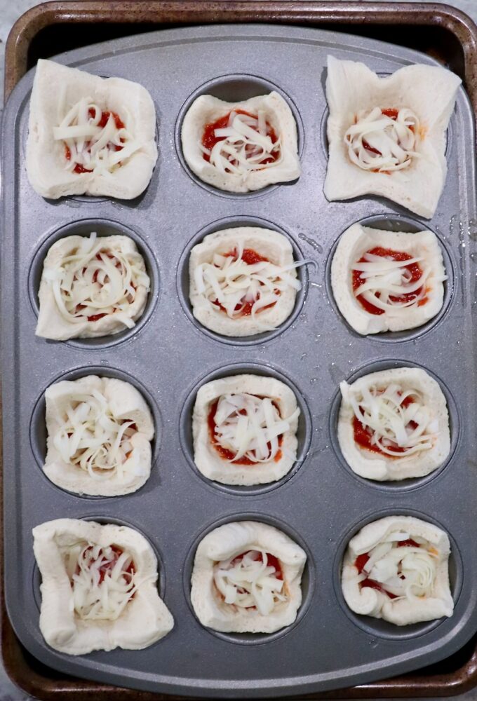 pizza dough squares pressed into a muffin tin and filled with marinara sauce and cheese