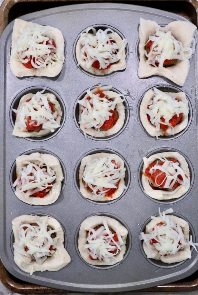 pizza dough squares pressed into a muffin tin and filled with marinara sauce, meatballs and cheese