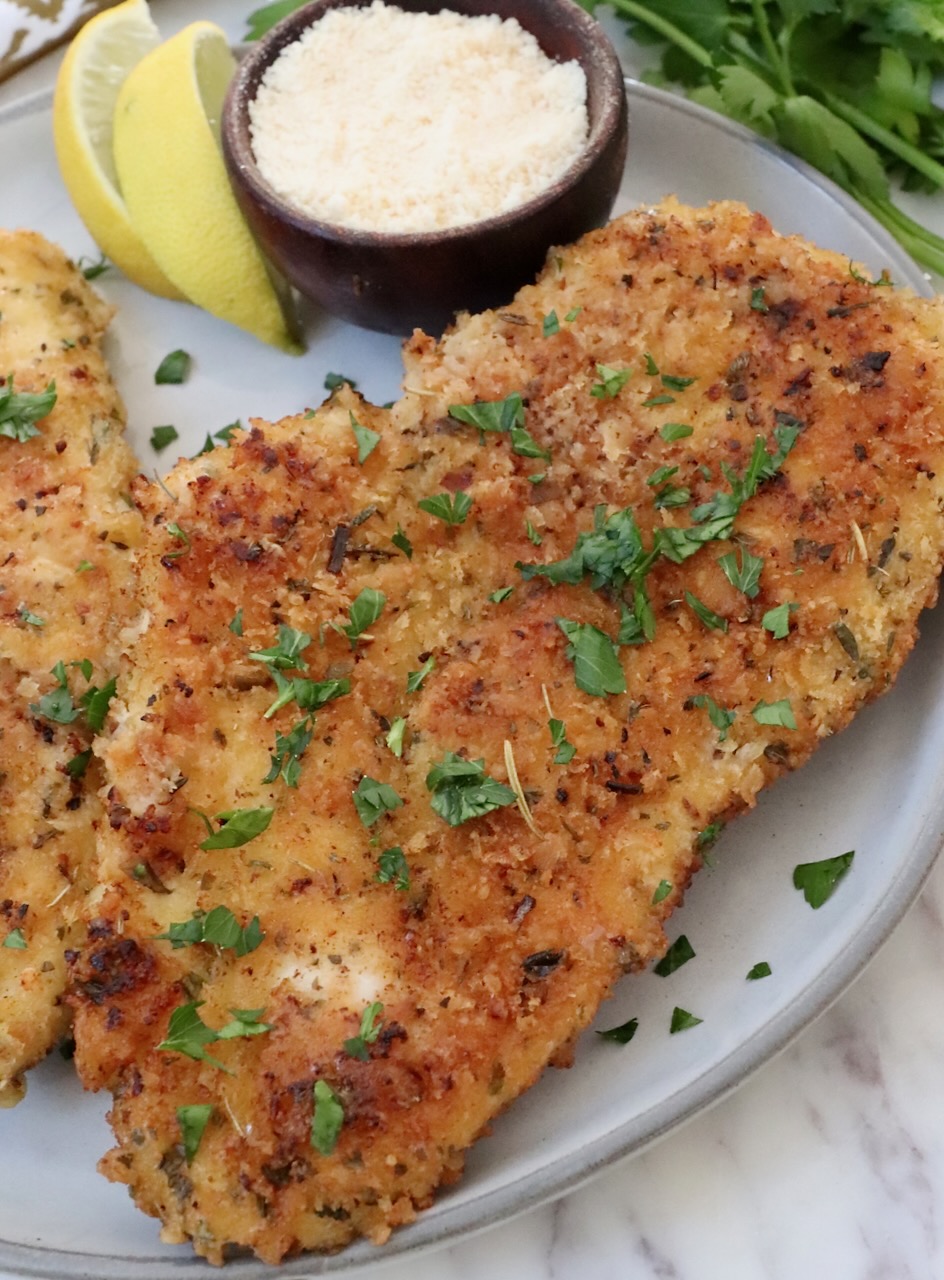 parmesan crusted chicken on a plate with lemon wedges