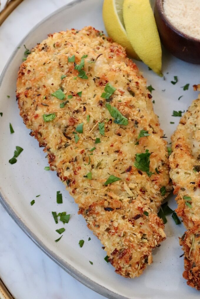 air fried parmesan crusted chicken breast on a plate with lemon wedges