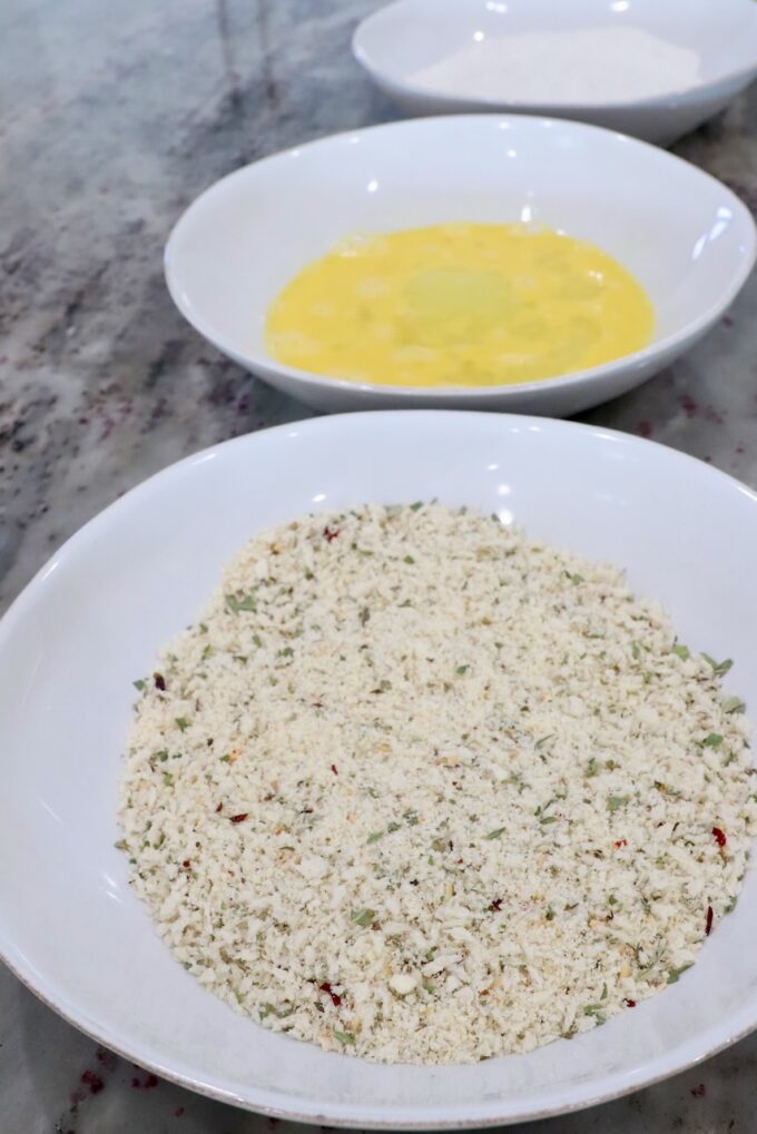 three bowls filled with seasoned breadcrumbs, whisked eggs and flour