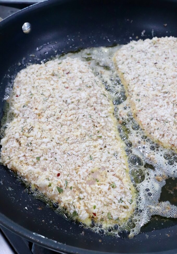 breadcrumb coated chicken breasts cooking in oil in a skillet