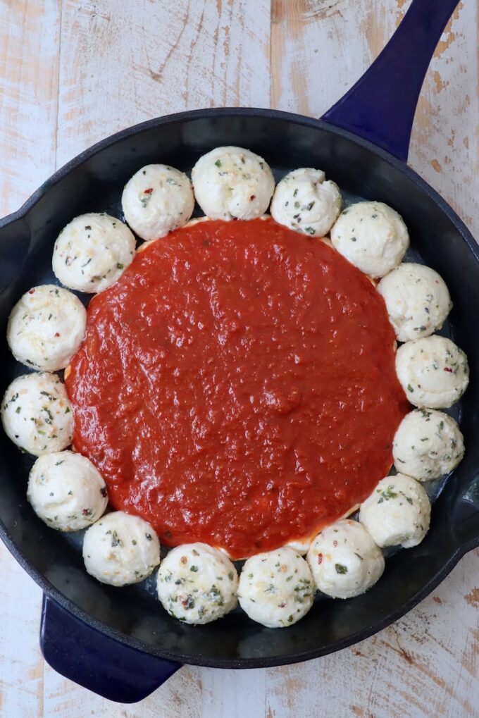 marinara sauce in the middle of a skillet surrounded by balls of dough