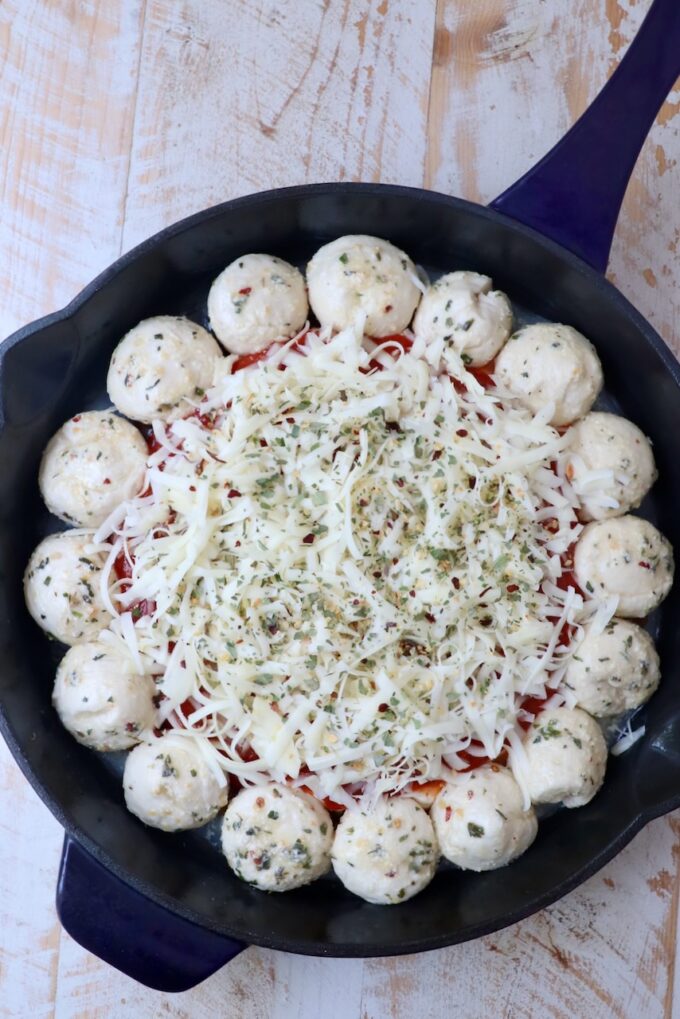 pizza dip in the middle of a skillet surrounded by balls of dough