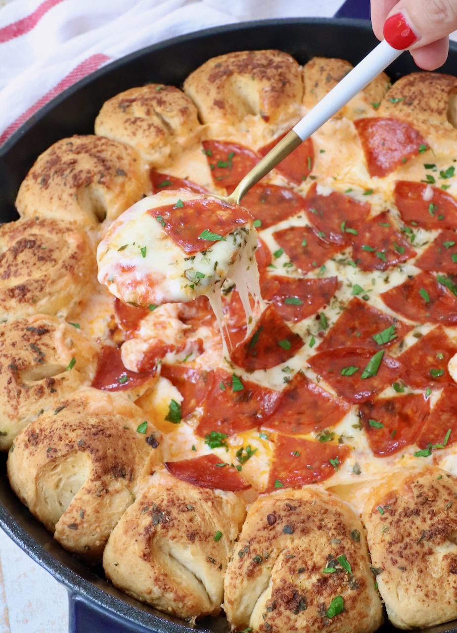 pizza dip in a cast iron skillet with pull apart bread around the outside and spoon scooping out the dip