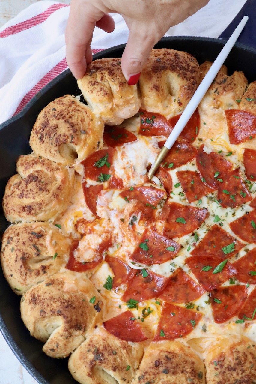 hand pulling piece of bread from a skillet with pizza dip