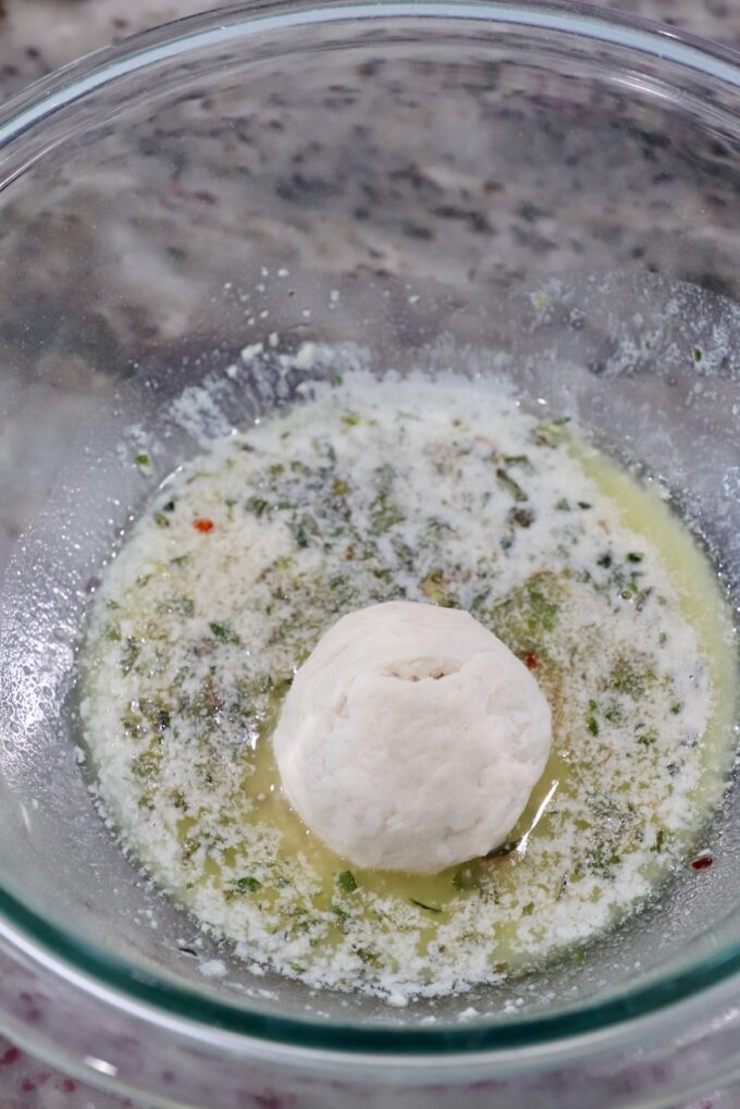 ball of biscuit dough rolled in melted butter with herbs in a glass bowl