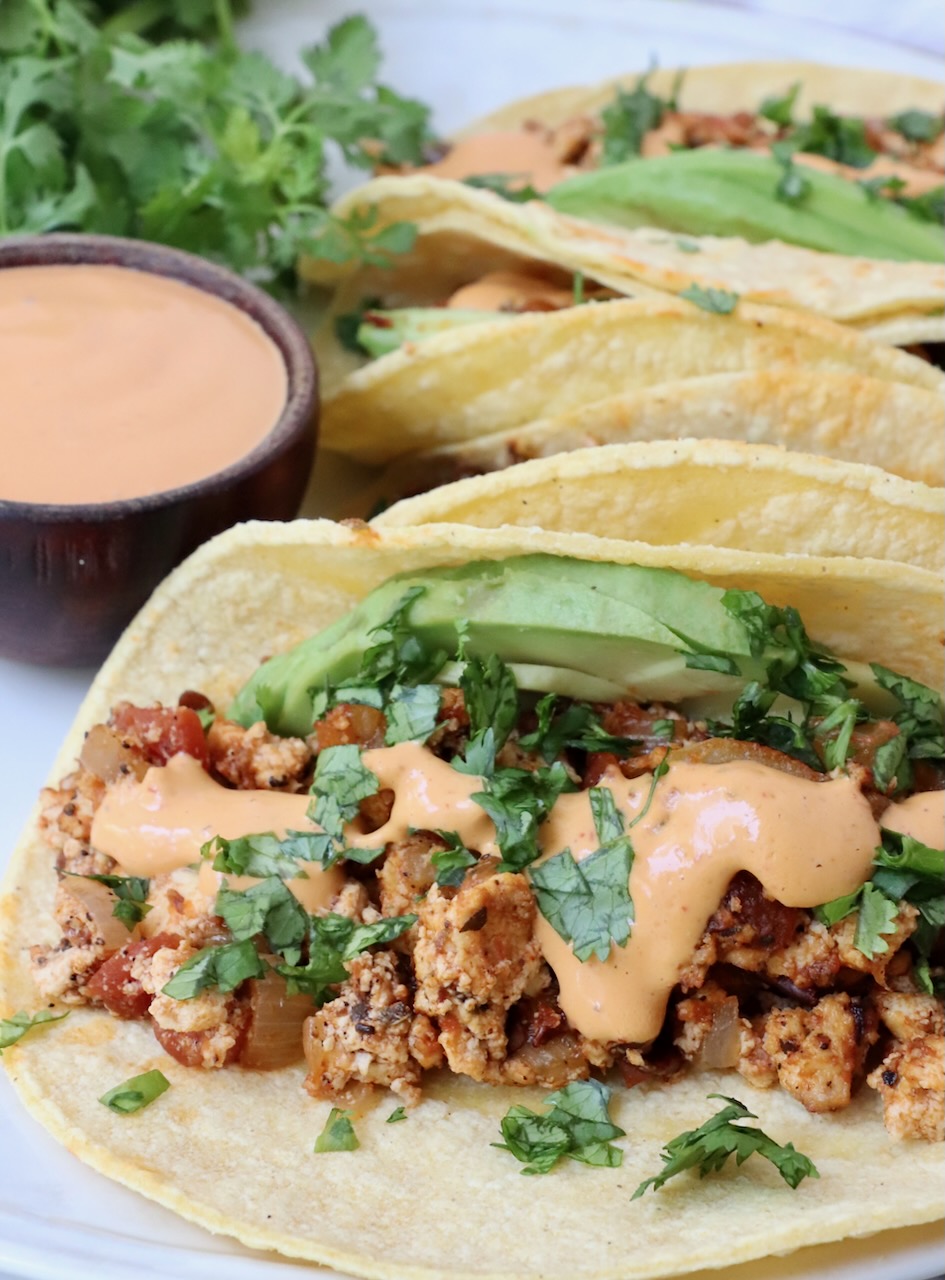 tacos on plate filled with crumbled tofu, chipotle sauce and avocado slices