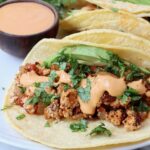 crumbled tofu taco topped with cilantro, avocado and chipotle sauce on a plate