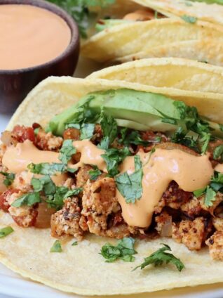 crumbled tofu taco topped with cilantro, avocado and chipotle sauce on a plate