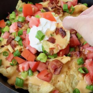 hand dipping chip into sour cream in a skillet of nachos