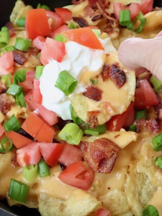 hand dipping chip into sour cream in a skillet of nachos