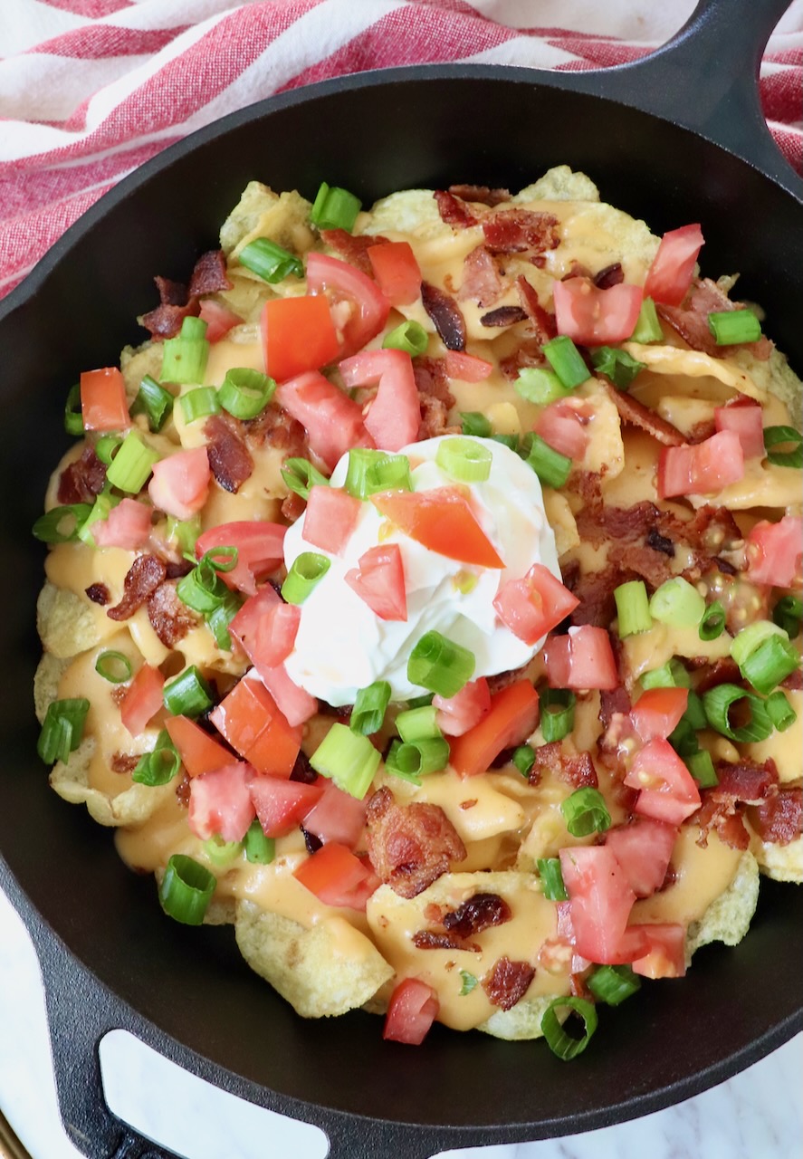 nachos topped with cheese sauce in a skillet with a dollop of sour cream in the middle