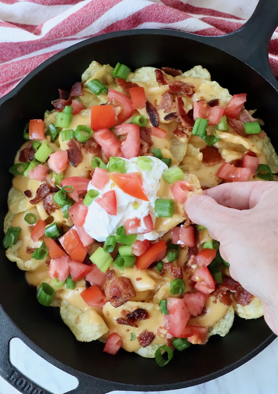 hand dipping chip into sour cream in a skillet of nachos