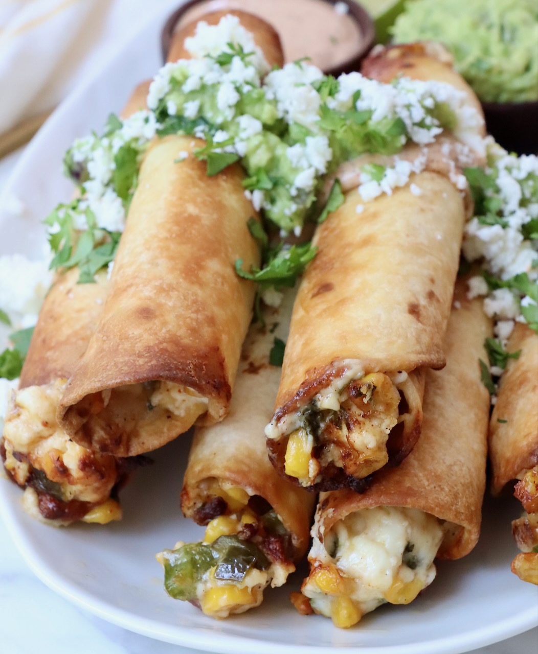 taquitos stacked up on a plate filled with cheese and corn