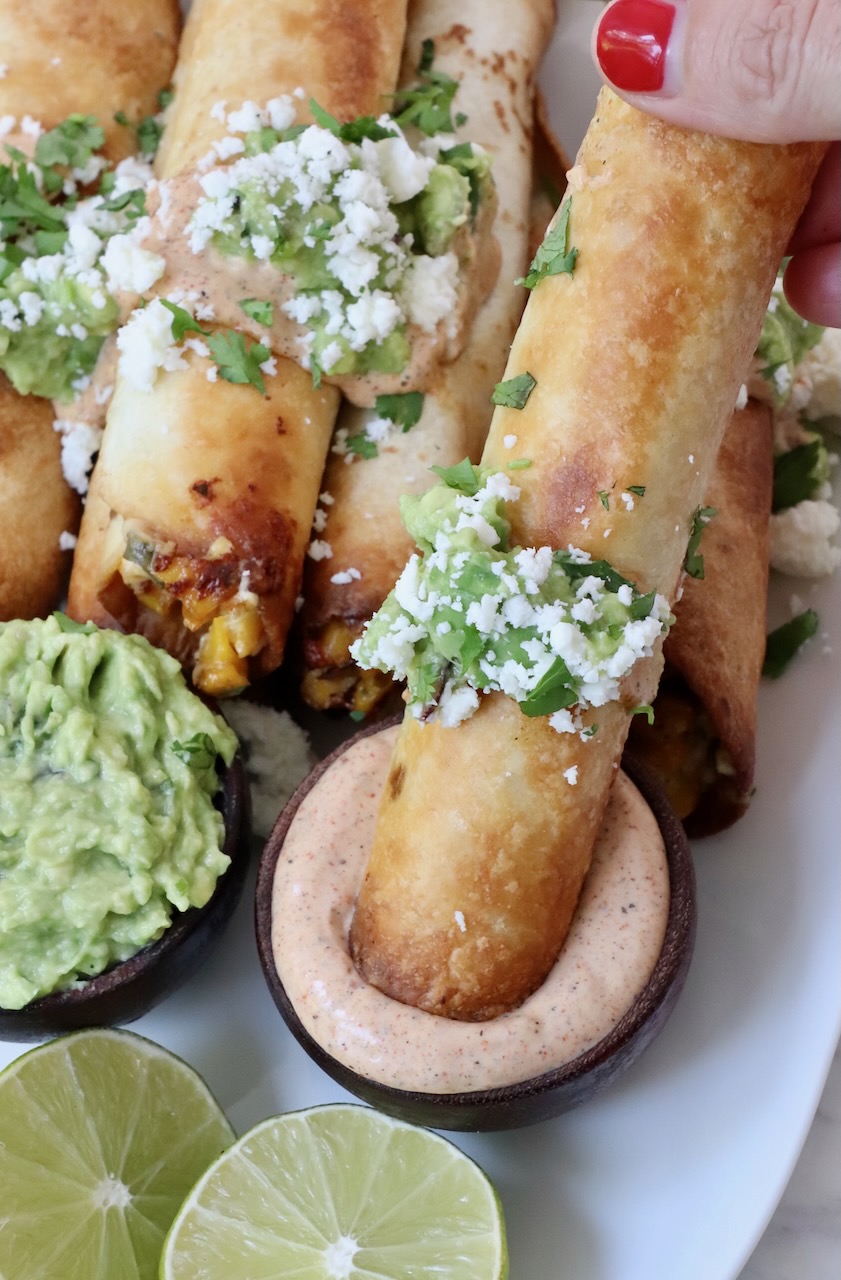 hand dipping taquito into a small bowl of chili lime sauce