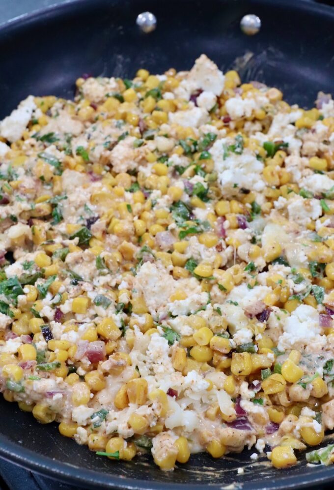 cooked corn tossed with cheese, cilantro and chili lime sauce in a skillet