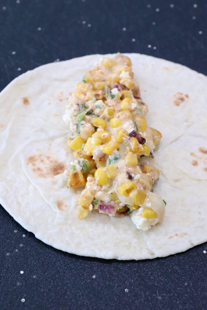 creamy corn mixture in the middle of a tortilla on a cutting board