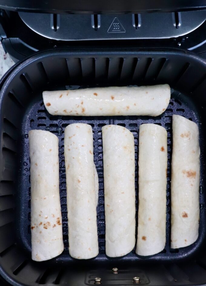 uncooked taquitos in an air fryer basket