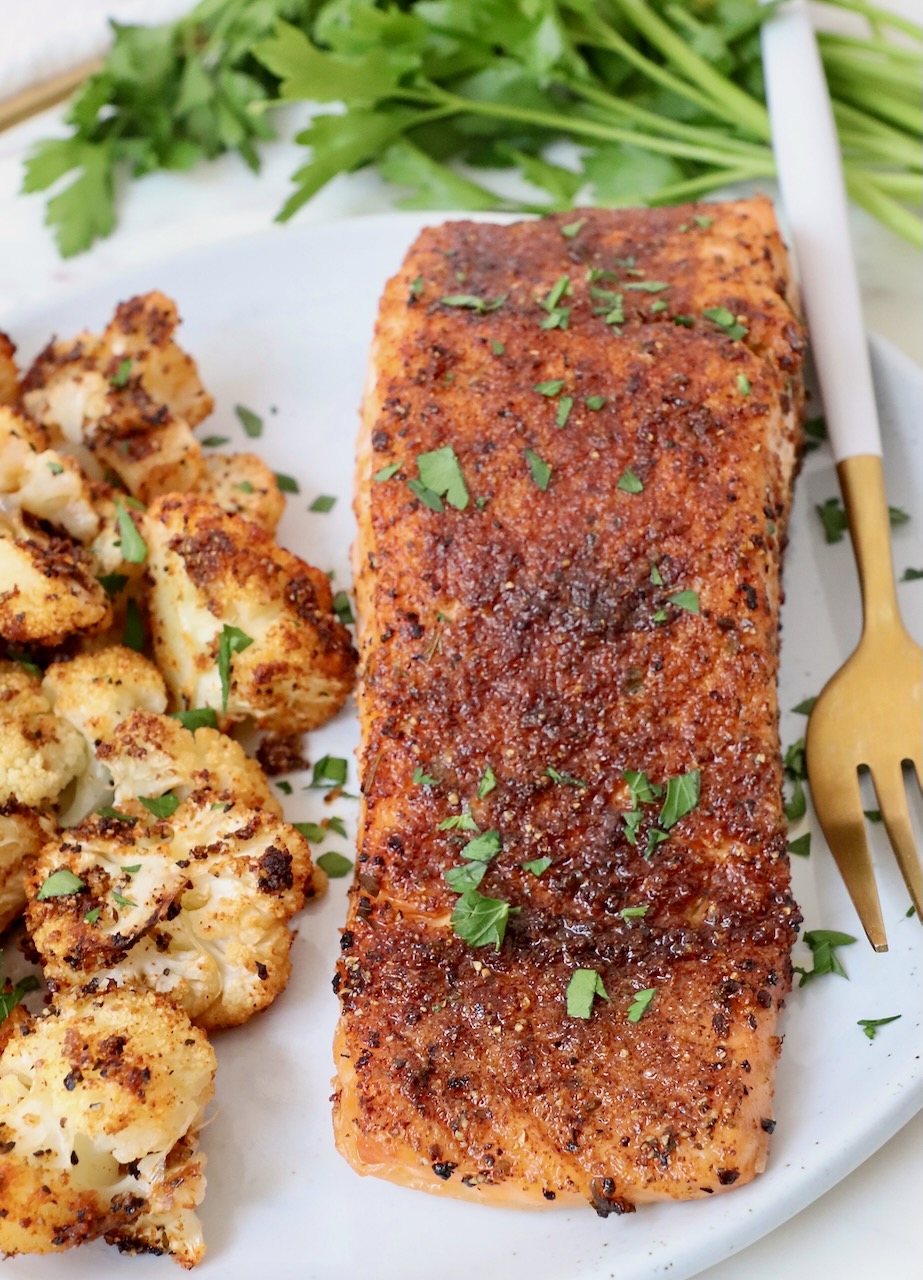 cooked, seasoned salmon on a plate with roasted cauliflower and a fork