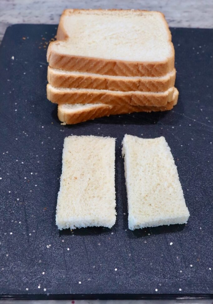 white bread stacked up on a cutting board with one piece sliced in half with the crusts removed