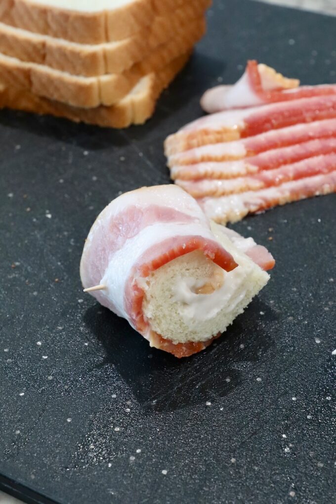 slice of bread rolled up in a slice of bacon, secured with a toothpick