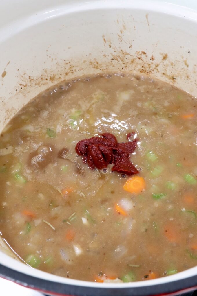 tomato paste on top of diced vegetables in chicken broth in a dutch oven