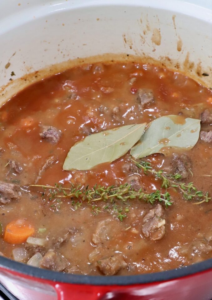 beef pot pie filling topped with thyme sprigs and bay leaves in a dutch oven