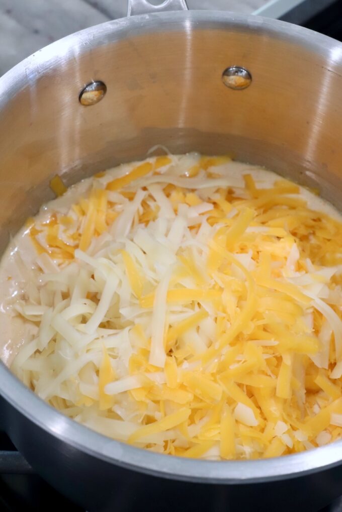 shredded cheese added to a creamy sauce in a pot on the stove