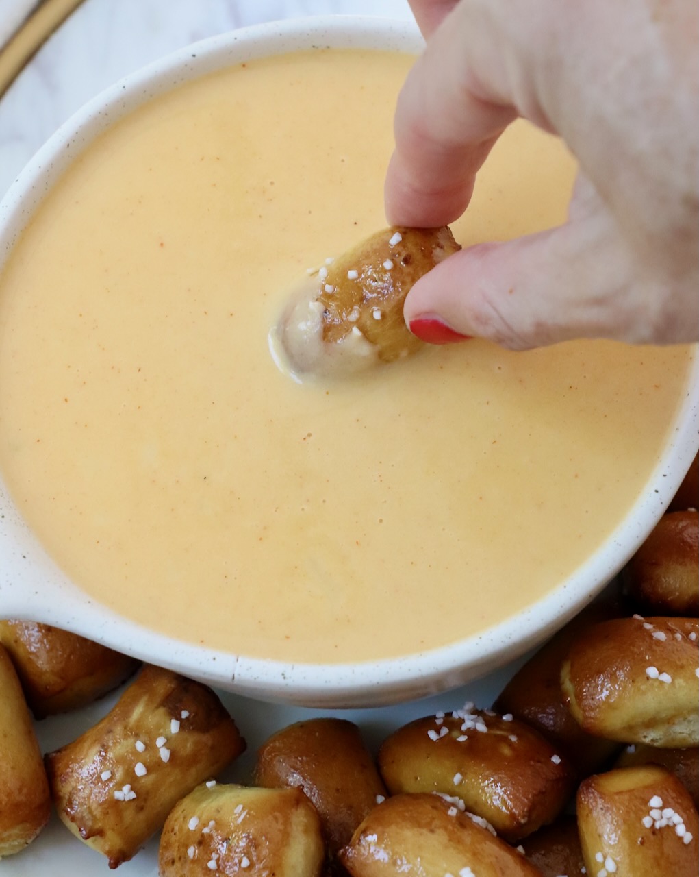 hand dipping pretzel bite into beer cheese dip