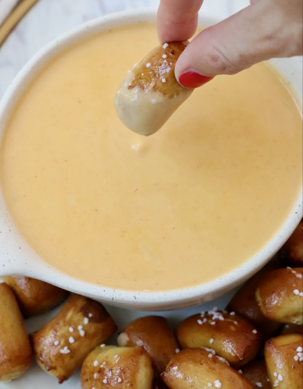 hand dipping pretzel bite into beer cheese dip in a bowl