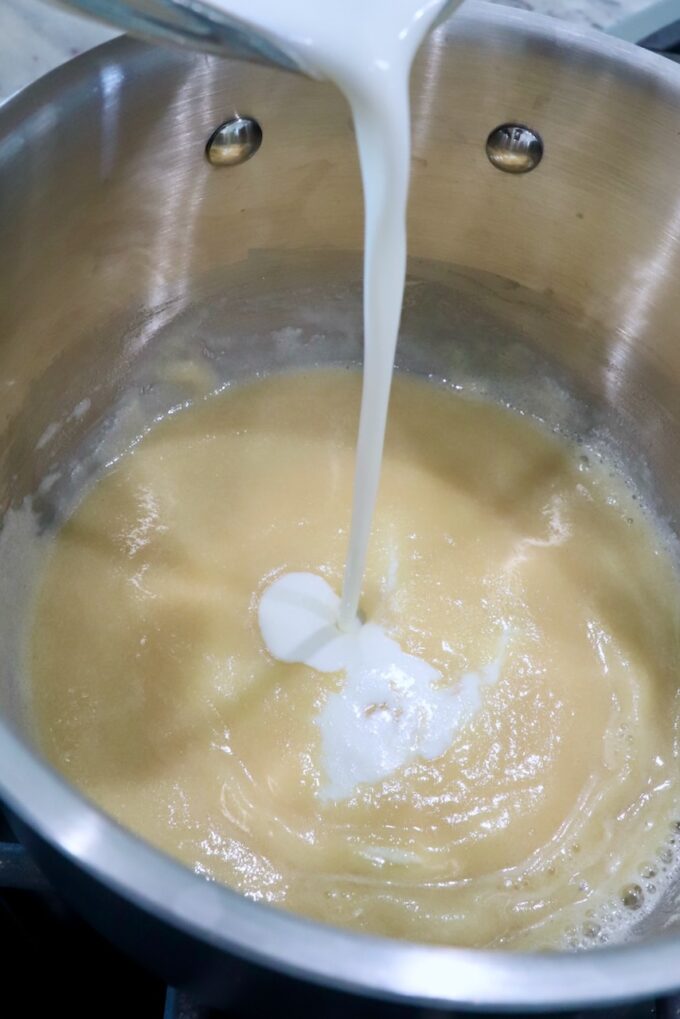 heavy cream poured into a roux in a pot on the stove