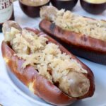 grilled bratwurst in a bun topped with sauerkraut on a plate