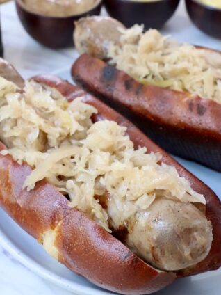 grilled bratwurst in a bun topped with sauerkraut on a plate