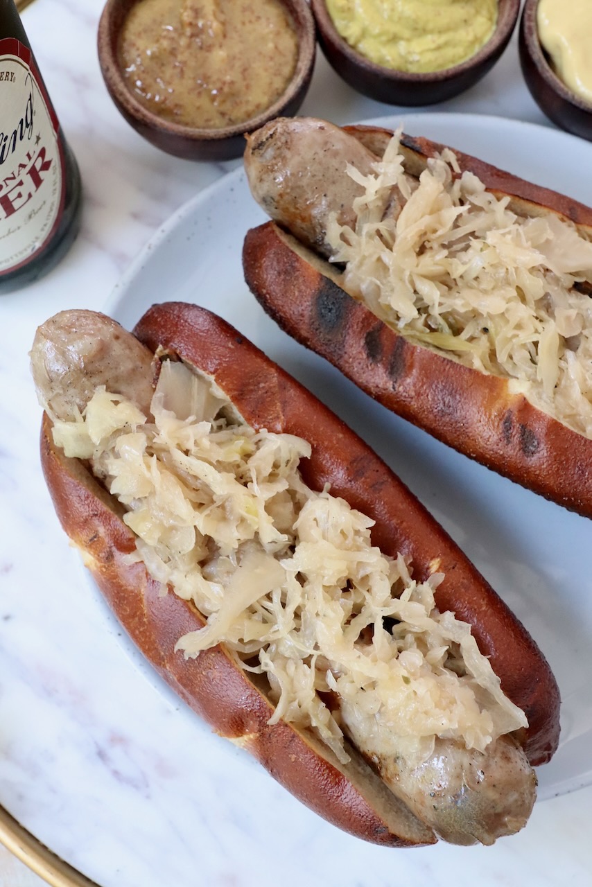 grilled bratwurst in pretzel bun topped with sauerkraut on a plate