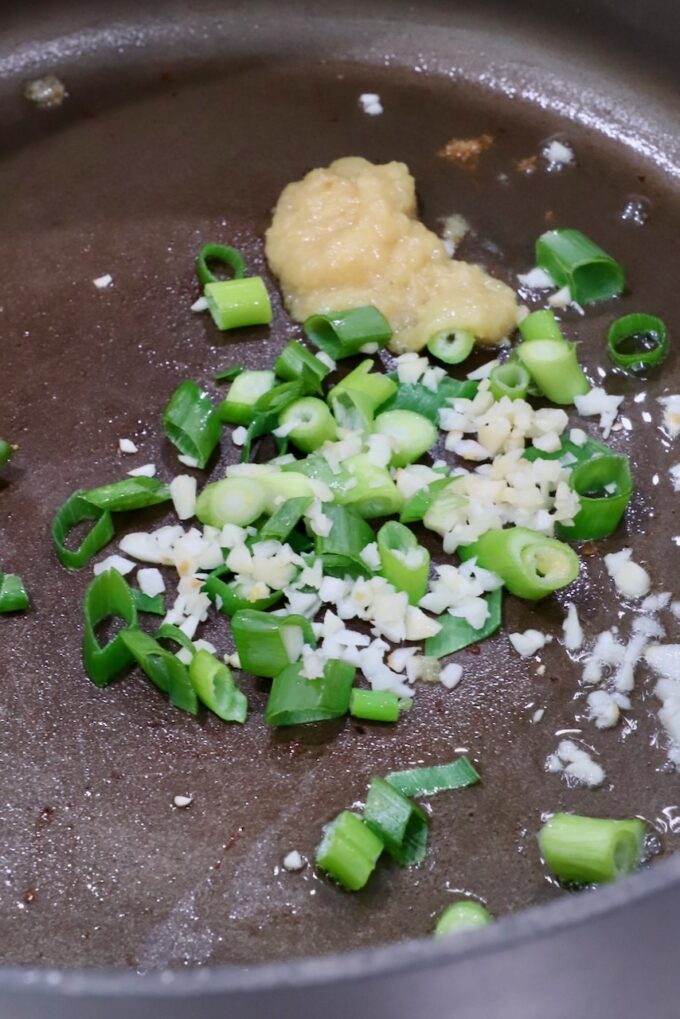 diced green onions, minced garlic and ginger paste in a pot on the stove